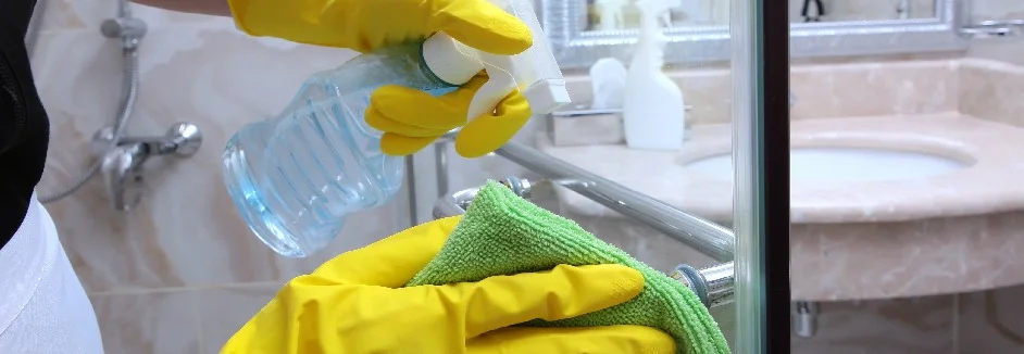 Person reinigt Duschtür mit Lappen.